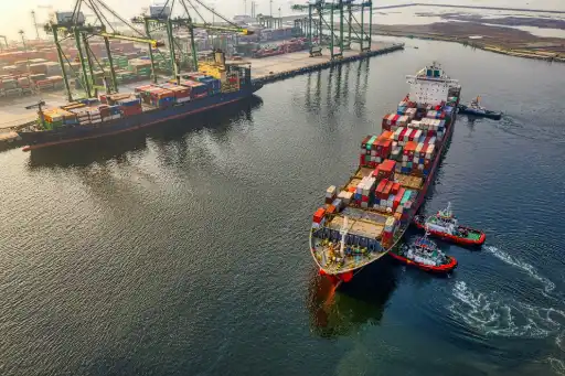 Barco de carga en el agua y en el puerto con contenedores de tu mercancia para tu negocio